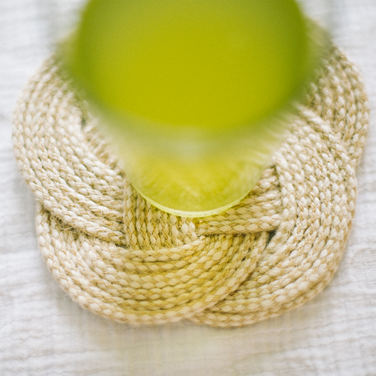 Braided rope coaster with a green glass, on a textured white surface, travel accessory
