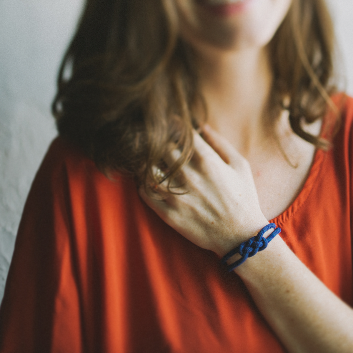 Woman in red shirt wearing a blue knotted bracelet, close-up on wrist and casual style.