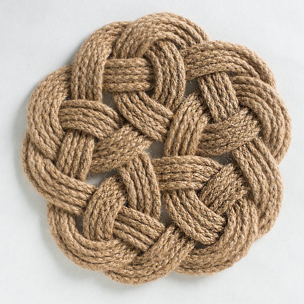 Round woven jute rope coaster with intricate knot design on white background